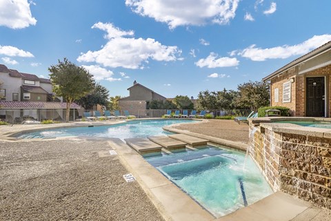 A pool with a stone wall and a building in the background.