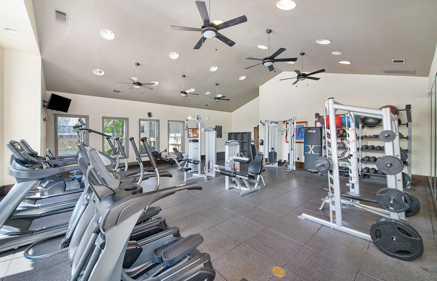 a gym with cardio equipment and ceiling fans