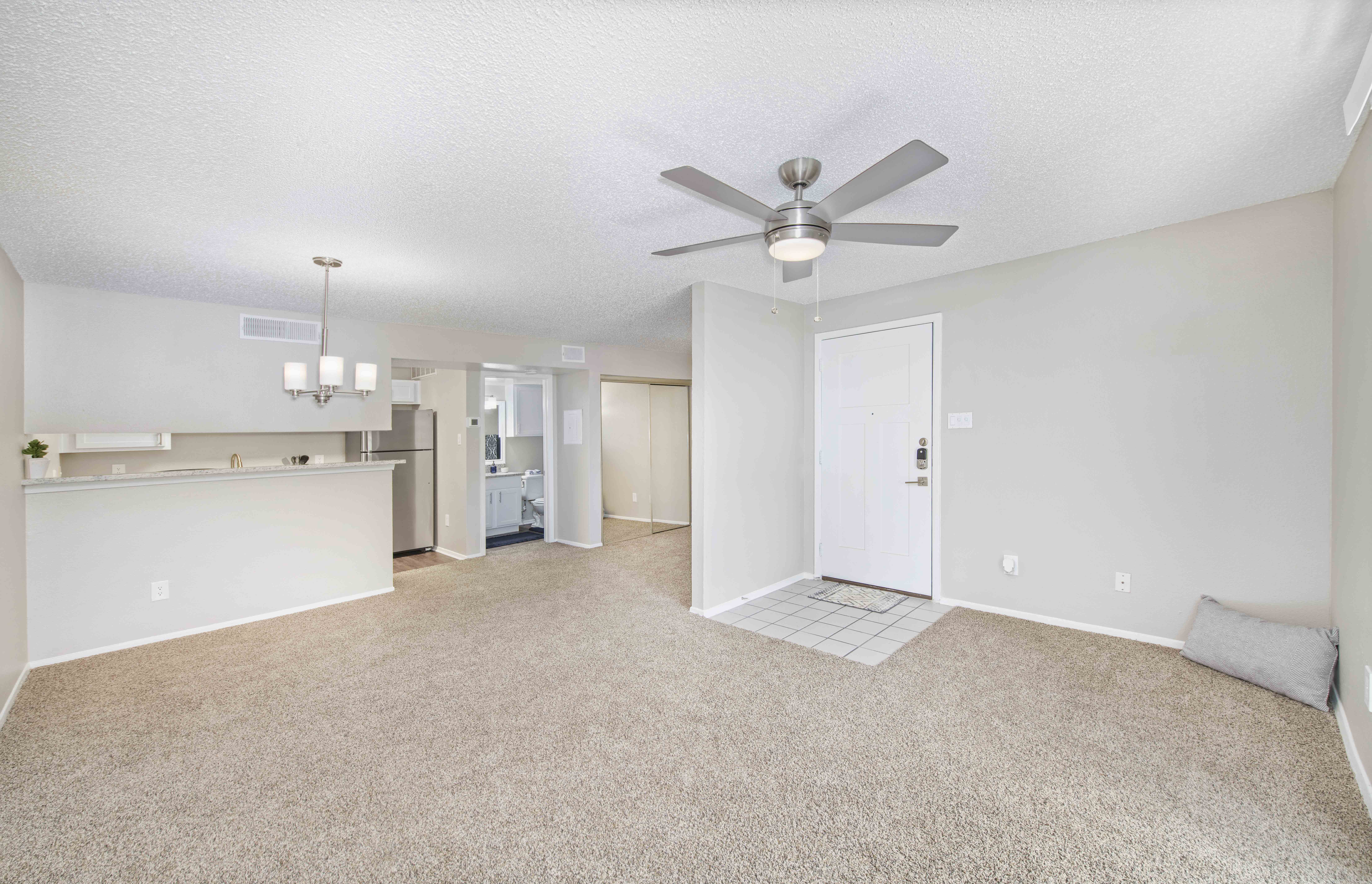 an empty living room with a ceiling fan and a kitchen