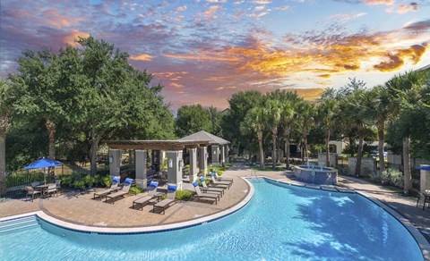 a swimming pool with lounge chairs and a fountain at sunset