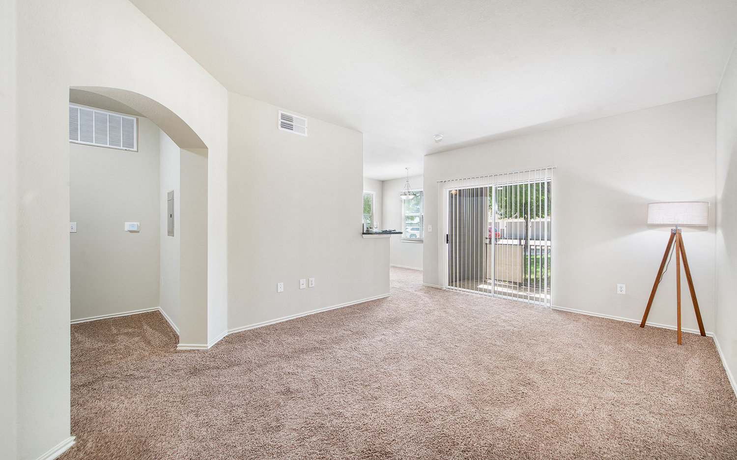 the living room and dining room of an apartment with carpeting and a glass door
