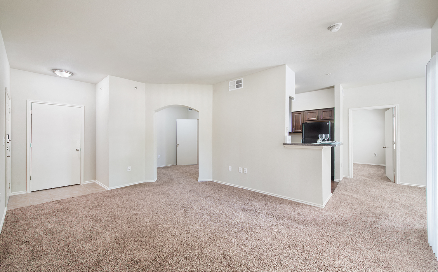an empty living room and kitchen with a carpeted floor