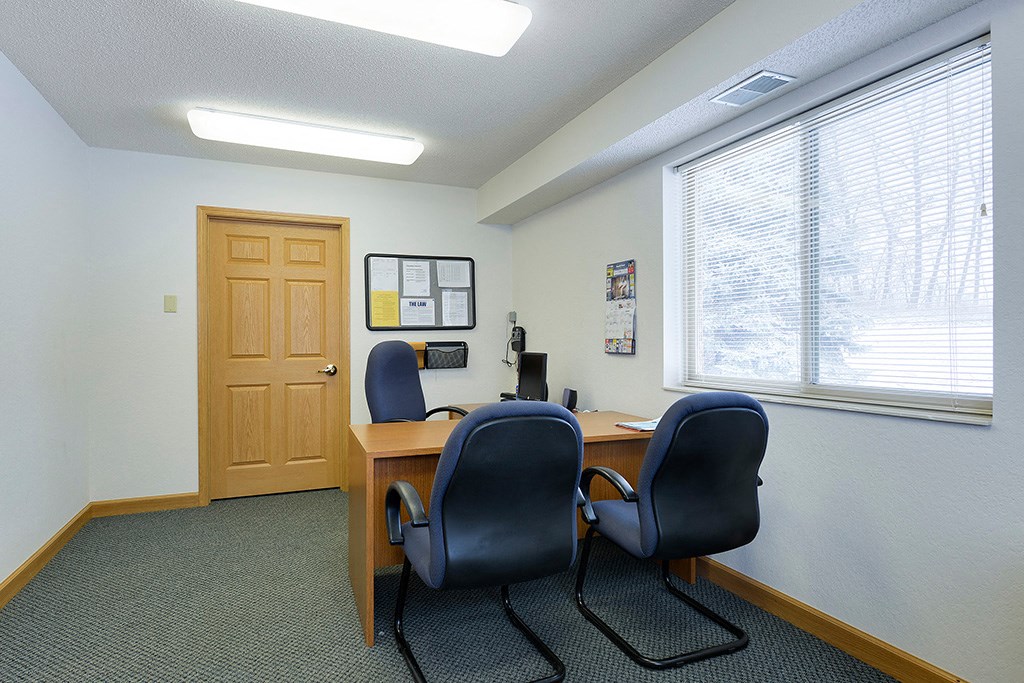 a room with a desk and chairs in front of a window