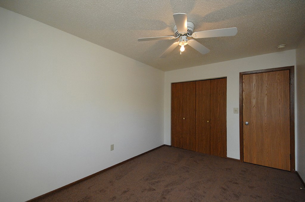 an empty living room with a ceiling fan and a closet