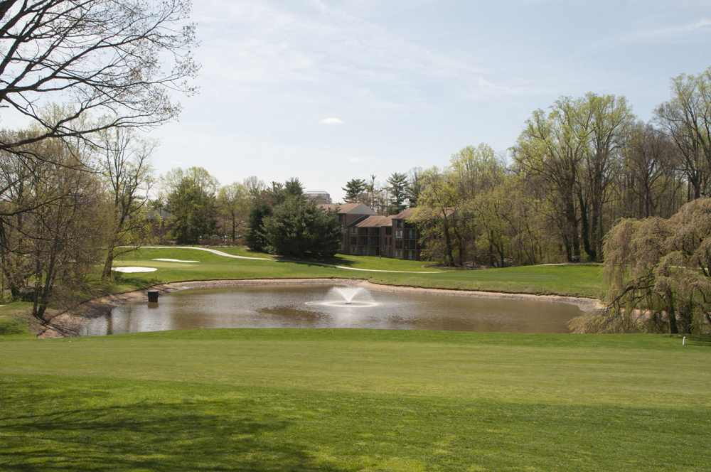 a golf course with a pond and a house in the background