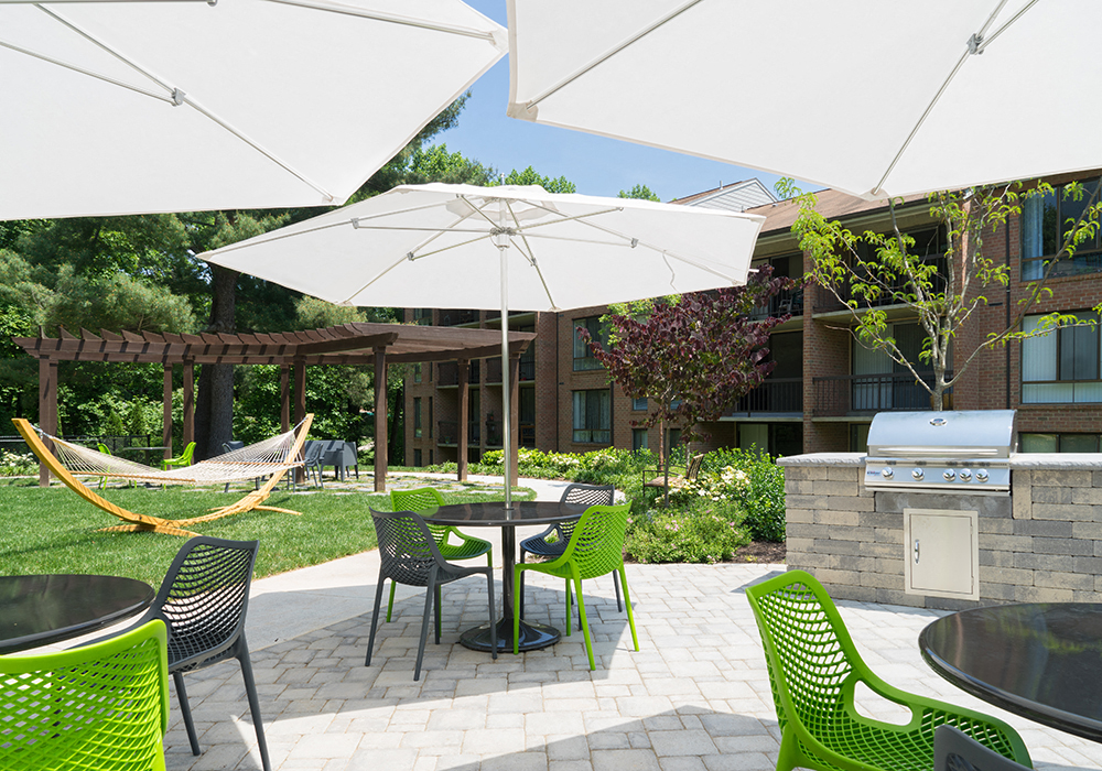 a patio with green chairs and umbrellas and a grill