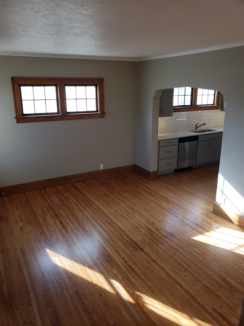 an empty living room with wooden floors and a kitchen