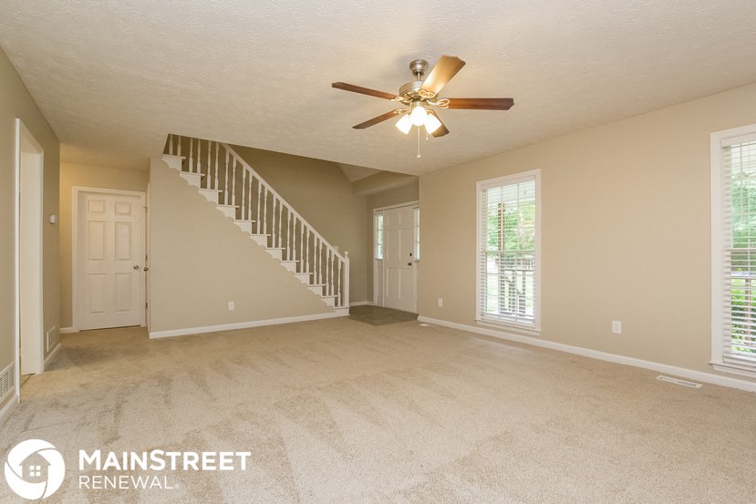 an empty living room with a ceiling fan and a staircase