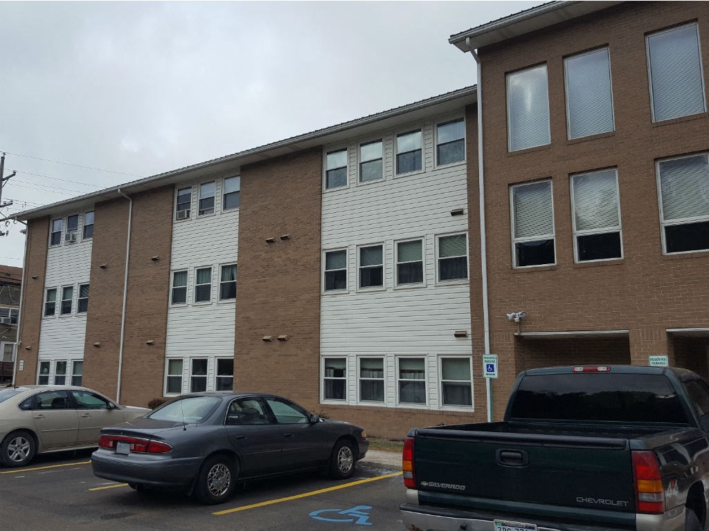 A black car is parked in a parking lot in front of a building.