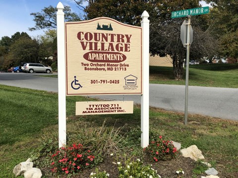 A sign for Country Village Apartment is displayed in front of a street sign.