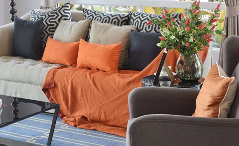 A living room with a grey couch, orange pillows, and a grey armchair.