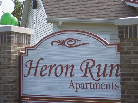 A sign for Heron Run Apartments is displayed in front of a house.