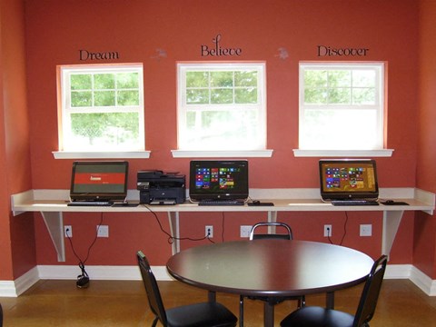 A room with a table, chairs and computers on a desk.