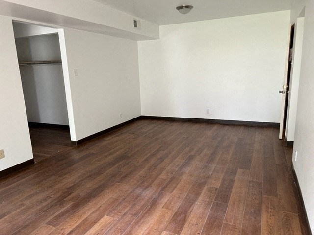 an empty living room with wood floors and a refrigerator