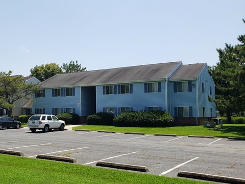 A white car is parked in a parking lot in front of a blue building.