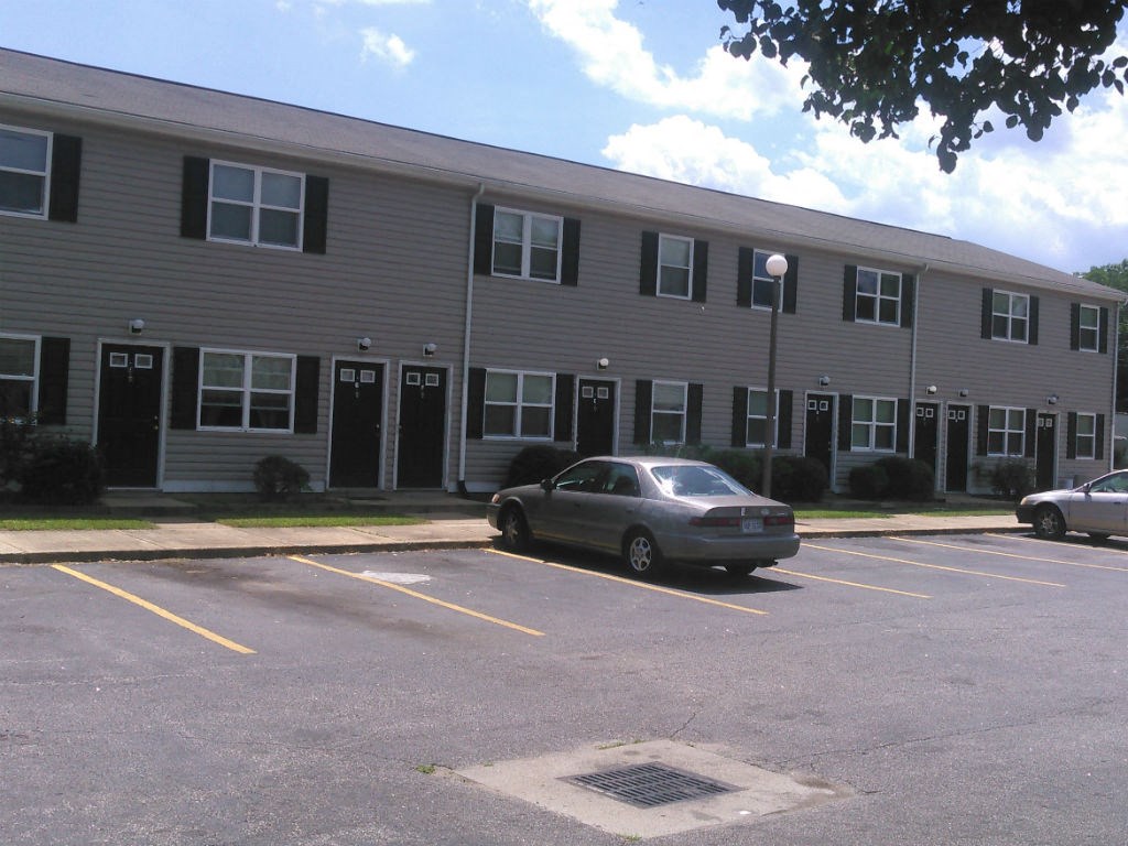 A grey car is parked in a parking lot in front of a grey building.