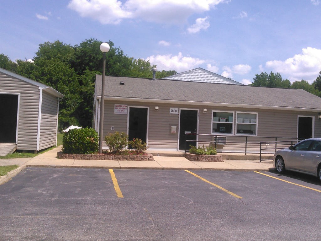 A grey building with a parking lot in front.