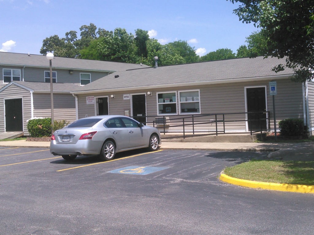 A grey car is parked in a parking lot in front of a grey building.