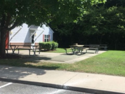 A park with picnic tables and a house in the background.