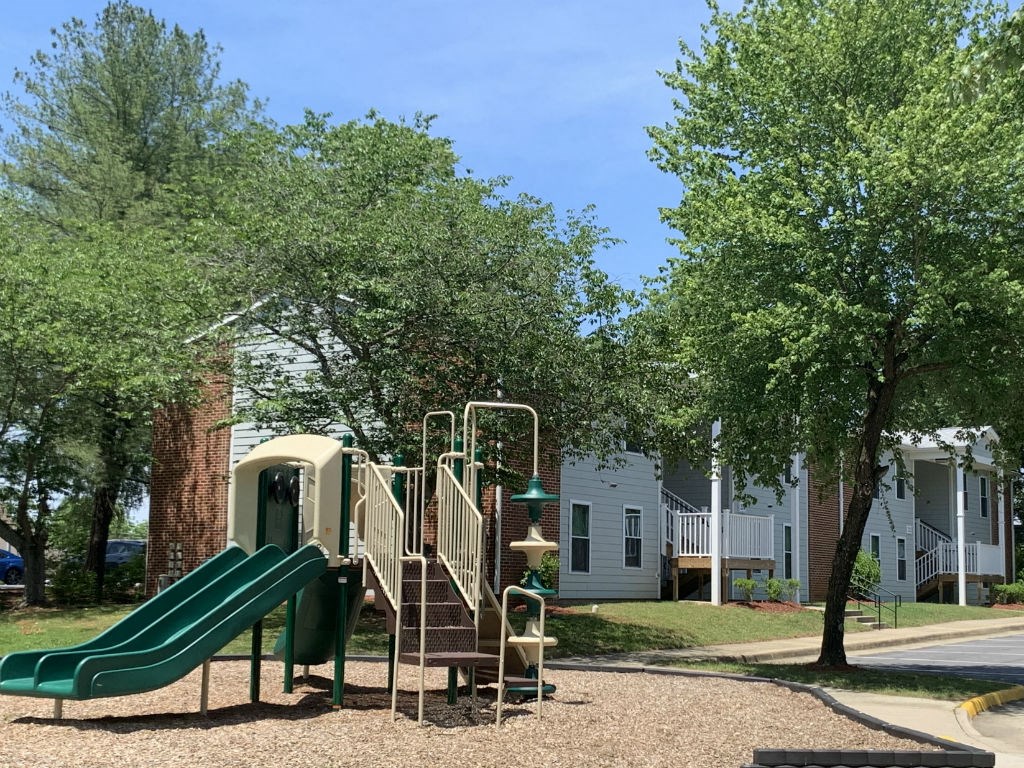 a playground with a slide and playset in front of a house