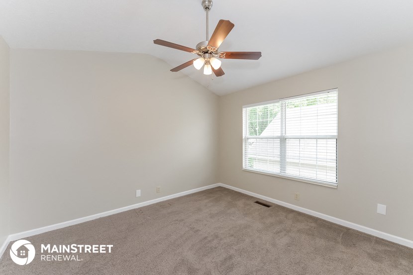 the spacious living room with ceiling fan and carpeting