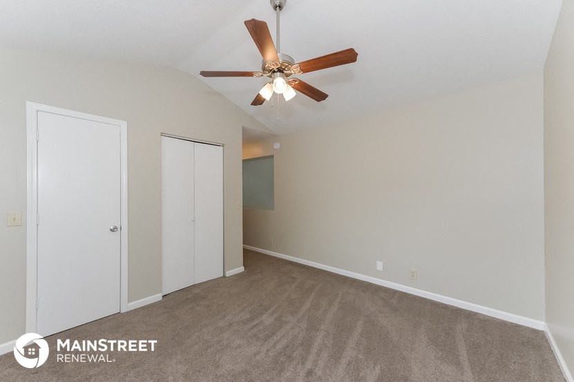 the spacious living room with ceiling fan and carpeting