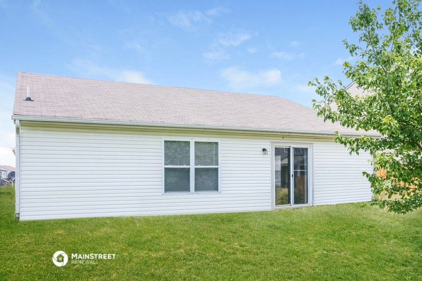 the backyard of a white house with a lawn and a tree