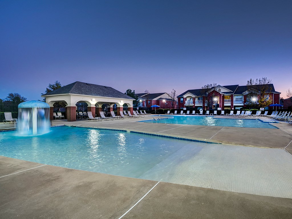 a swimming pool at night with apartments in the background