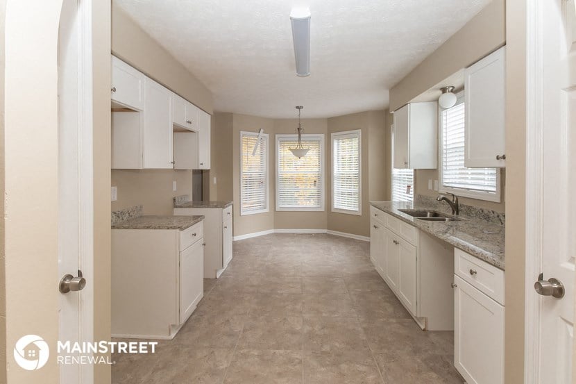 a large kitchen with white cabinets and counters and a large window