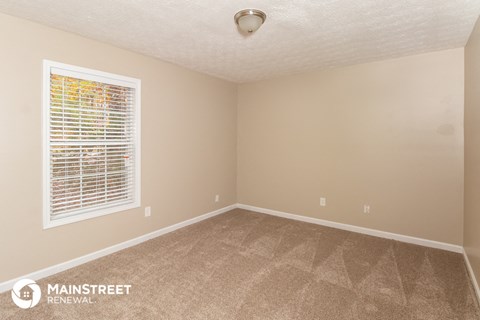 the spacious living room of this manufactured home has a large window and beige carpet