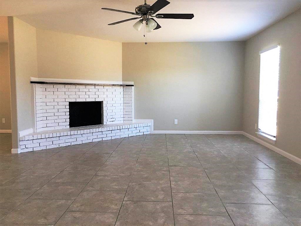 an empty living room with a brick fireplace and a ceiling fan