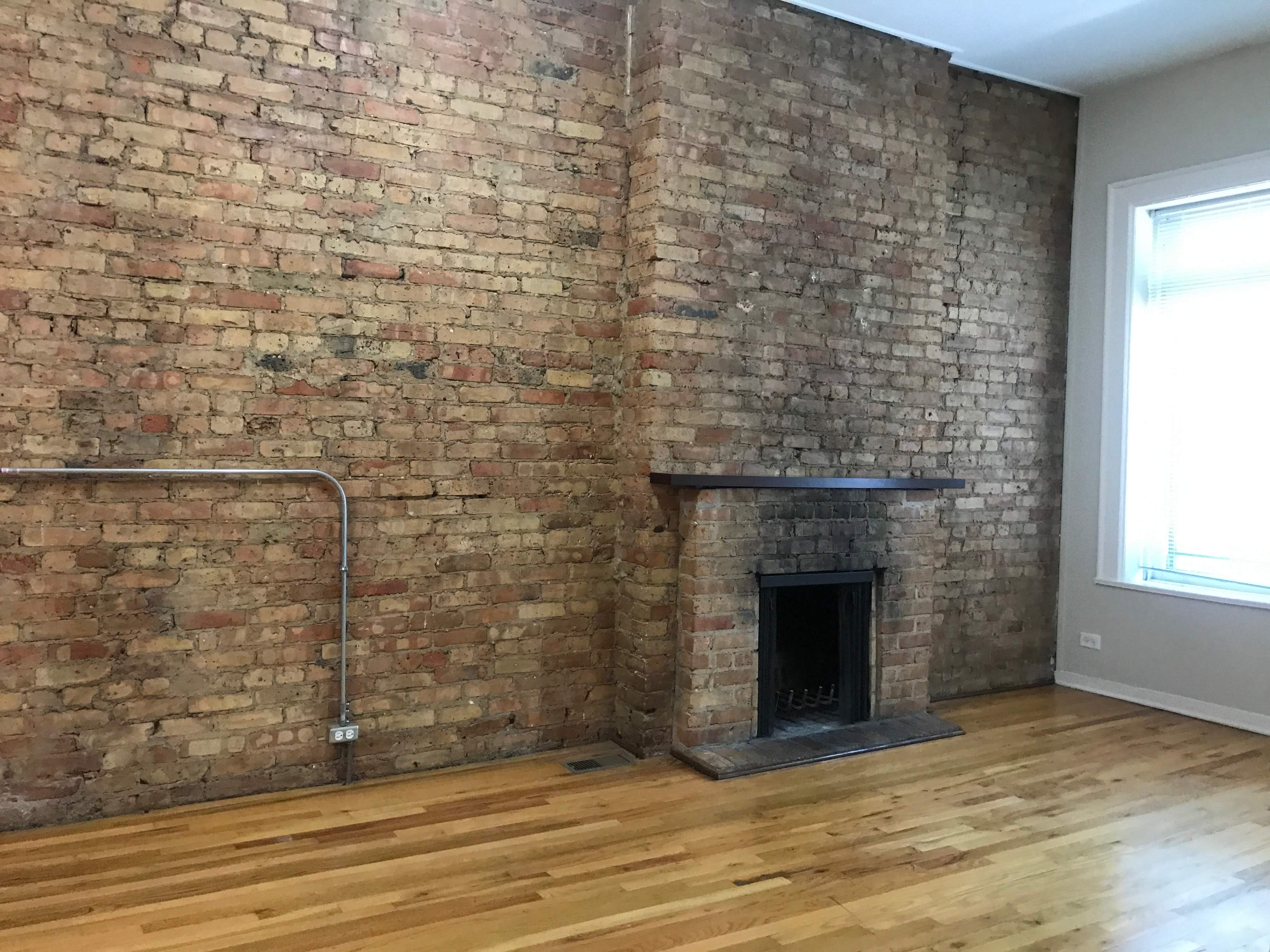 an exposed brick wall in a room with wooden floors and a fireplace