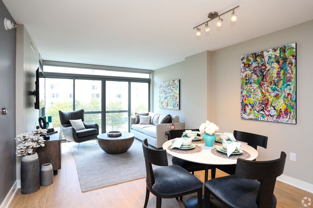 A dining room with a table set for six and a painting on the wall.