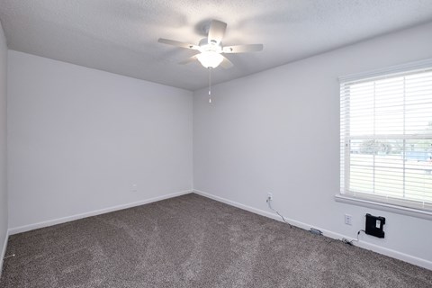 an empty bedroom with a ceiling fan and a window