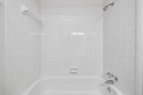 a white tiled bathroom with a tub and a shower