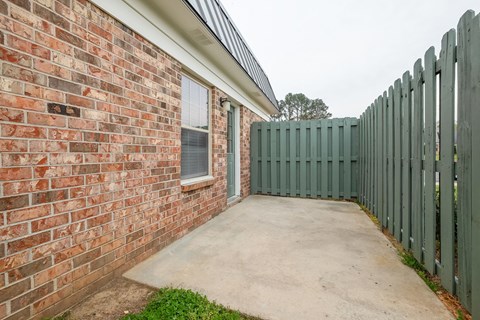 the side of a brick building with a concrete sidewalk and a fence