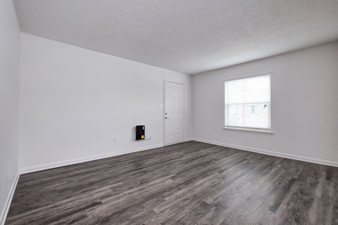 the living room of an apartment with wood flooring and a window