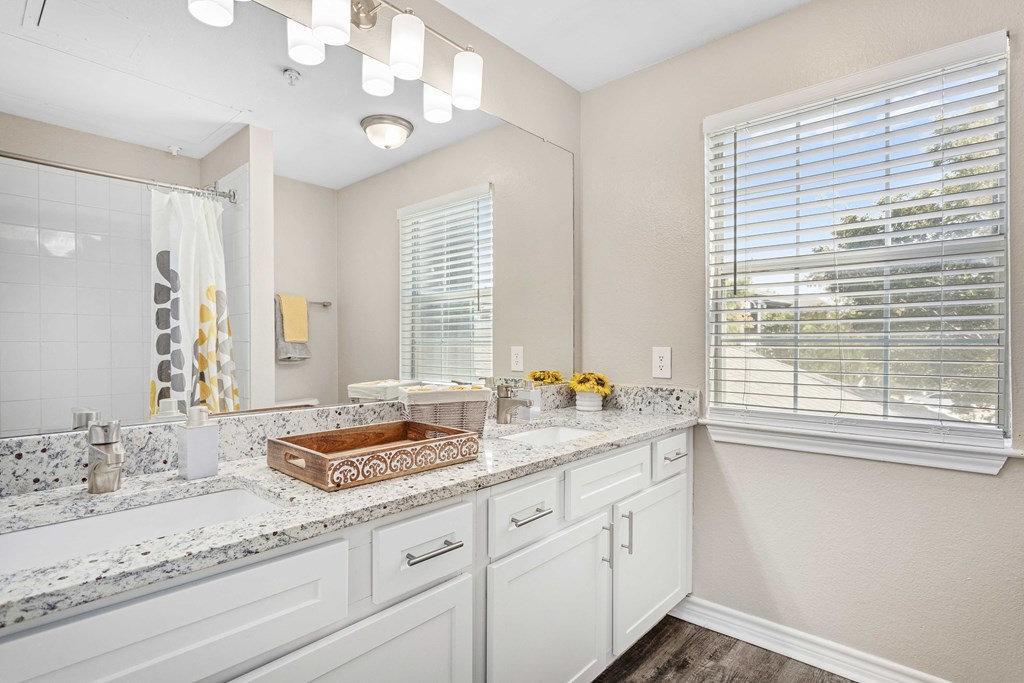 A bathroom with a marble counter top and white cabinets.