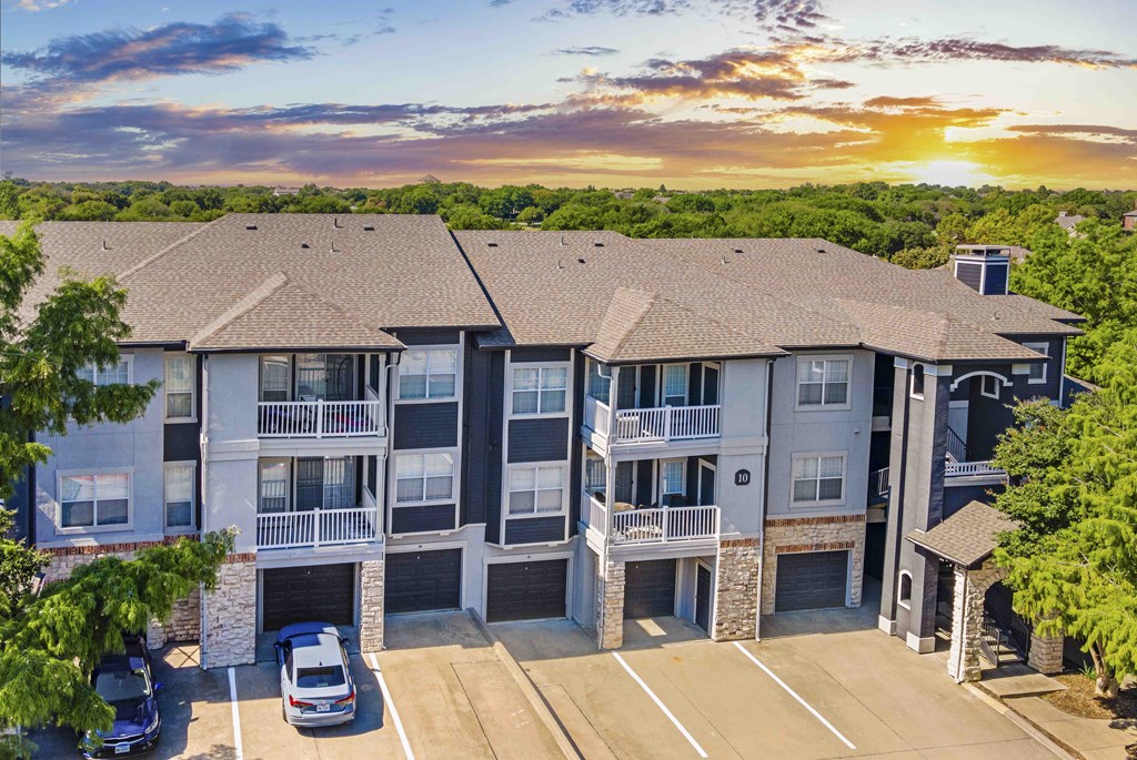 A sunset view of a multi-story apartment building with cars parked in the driveway.