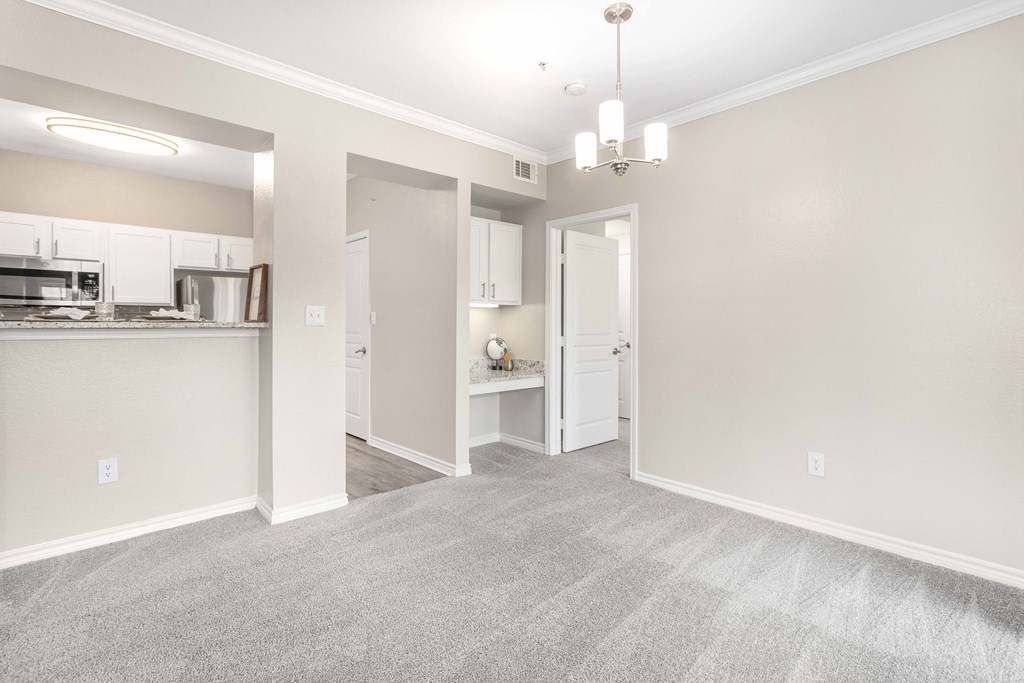 A spacious kitchen and living room with white appliances and a grey carpet.