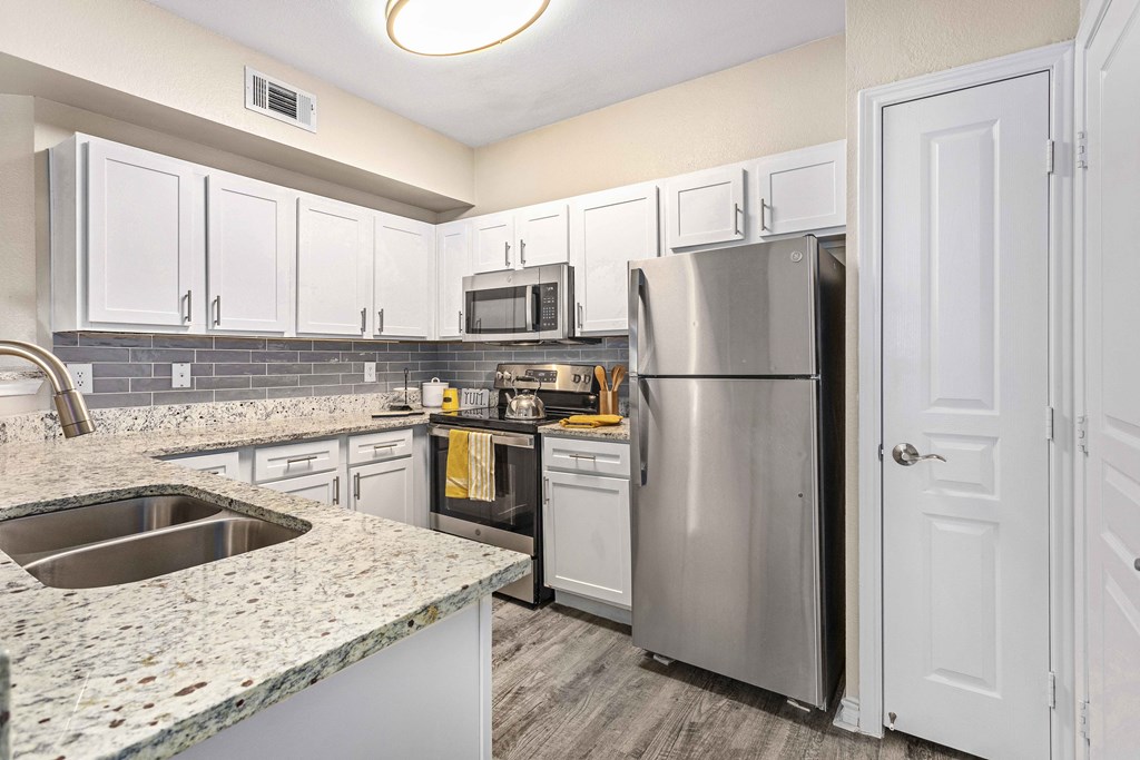 A kitchen with a stainless steel refrigerator and a granite countertop.