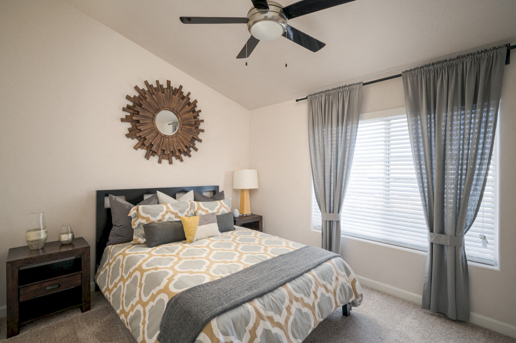 Model bedroom with wall to wall carpet, ceiling fans, queen bed, and large windows
