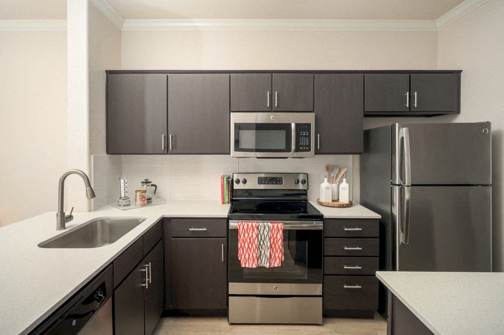 Model kitchen with dark brown cabinets, white quartz countertops, and stainless steel appliances