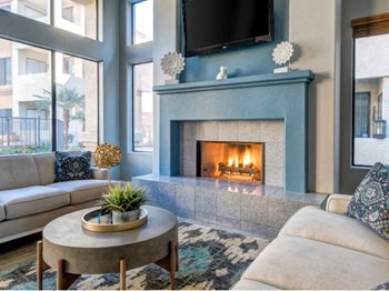Ingleside Apartments Clubhouse Sitting area with blue fireplace with tv above and beige couches - Photo Gallery 5
