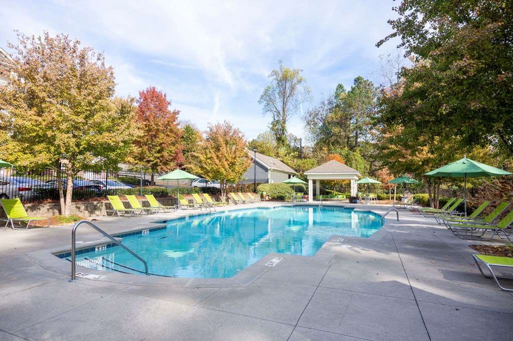 a resort style pool with chairs and umbrellas and trees