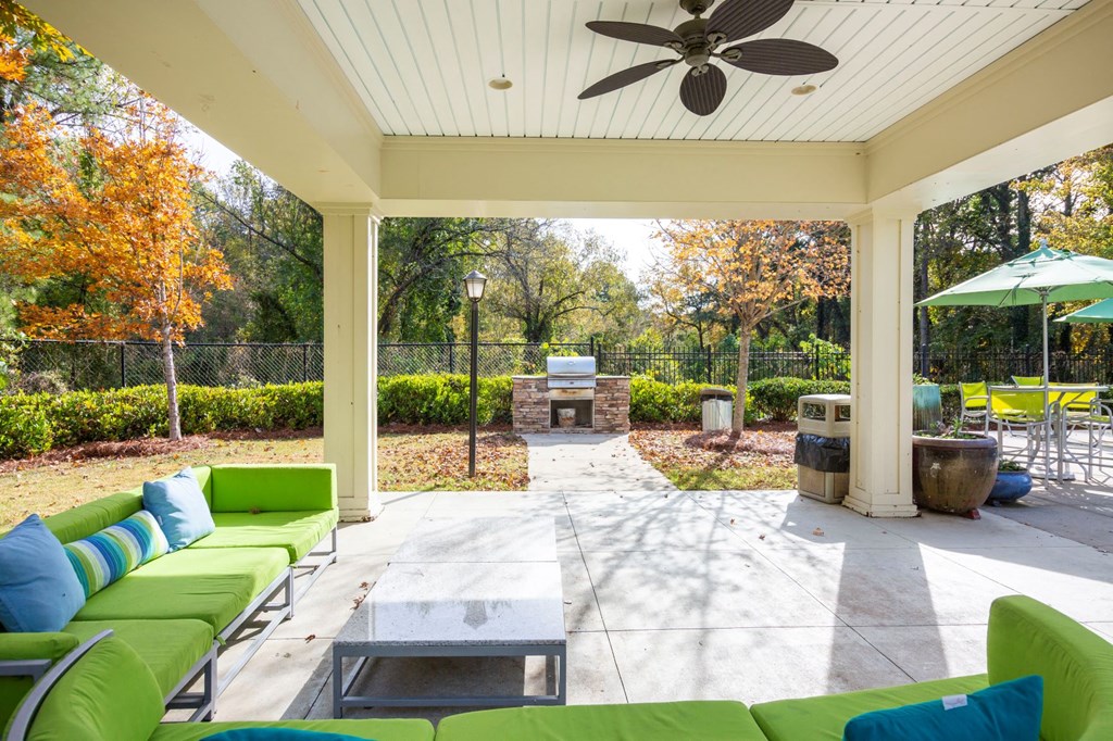 a covered patio with green couches and a fire pit
