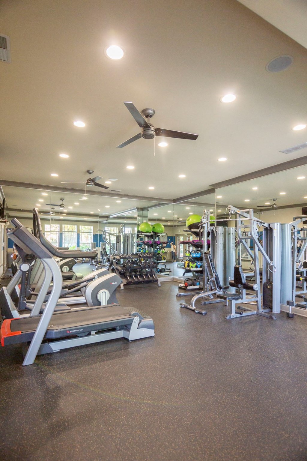 a gym with cardio equipment and a ceiling fan