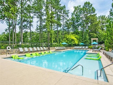 a swimming pool with green and white chairs    and trees