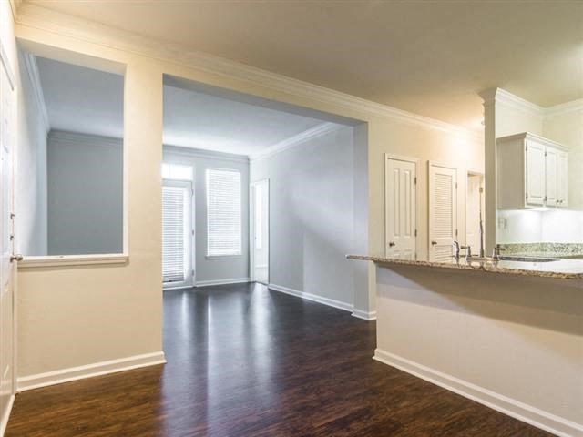 an empty living room with a kitchen and a hard wood floor