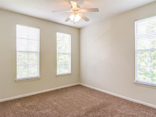 an empty room with a ceiling fan and three windows